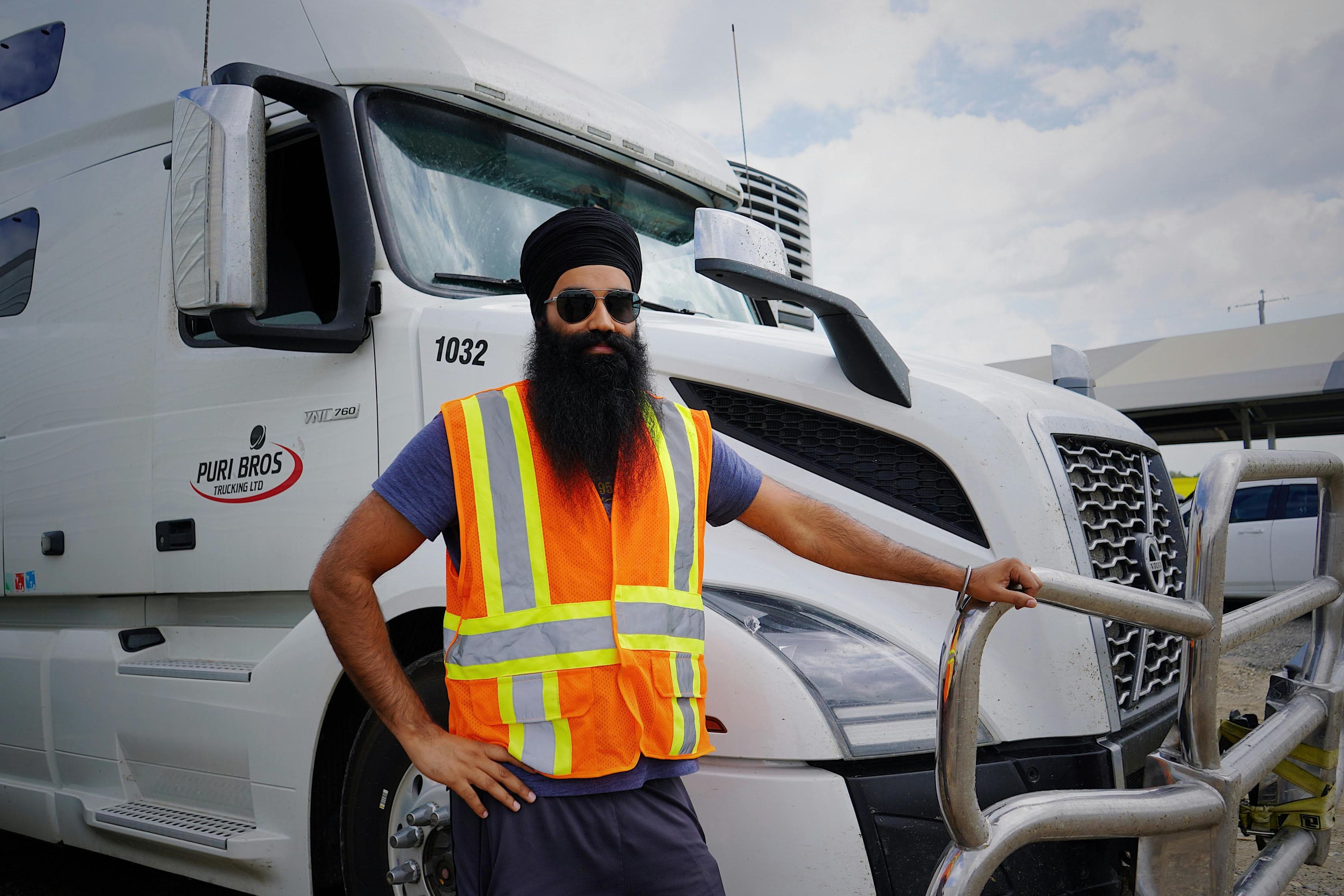 Sikh commercial truck driver in safety vest standing beside his freight vehicle
